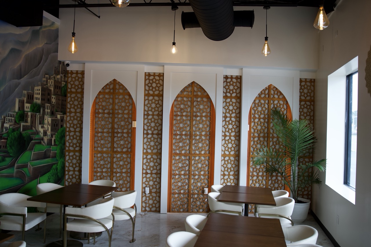 Daytime seating area — white chairs, walnut tables and the lit mashrabiya arches