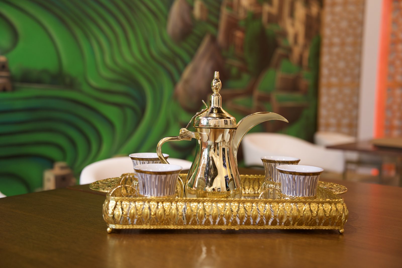 A gold dallah and cups before the green Yemeni mountain mural