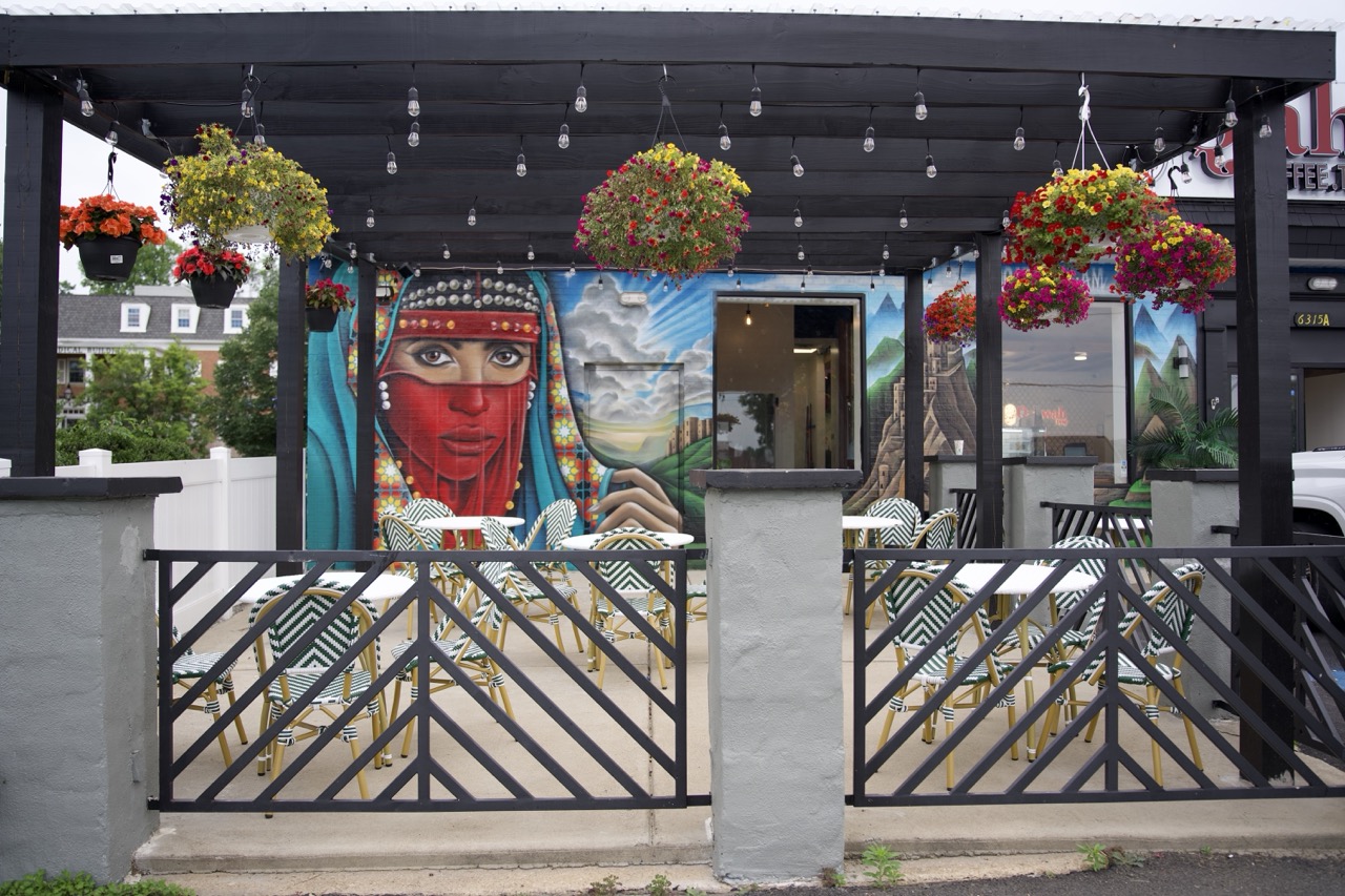 Qahwah Drip's covered patio with a Yemeni mural of a woman in a red veil beside a mountain village