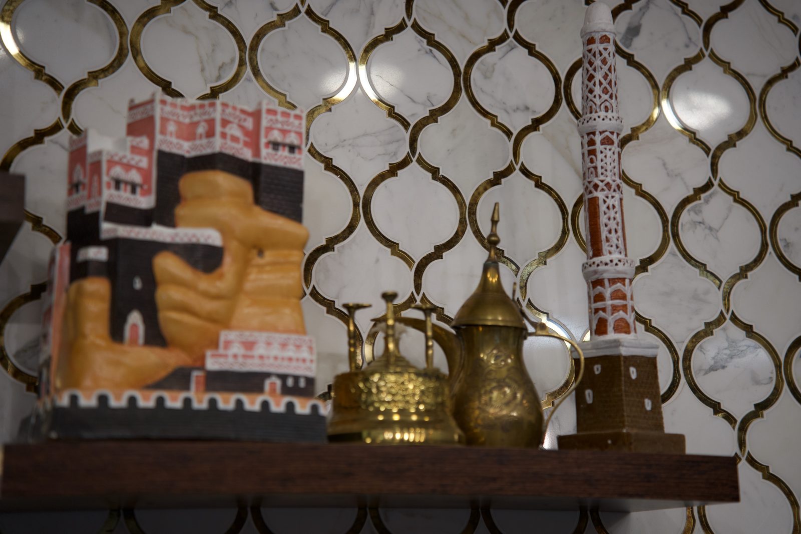 Hand-made clay models of Sana'a tower-houses and brass dallahs on the brass-lattice marble wall