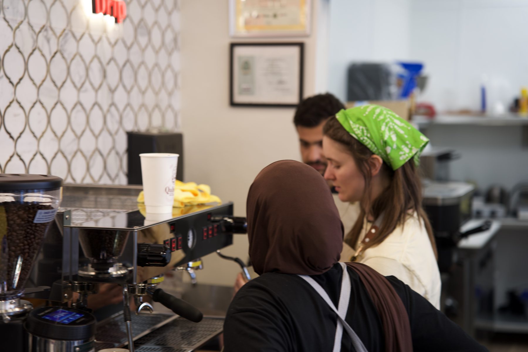 The Qahwah Drip team crafting drinks at the espresso bar beneath the logo wall