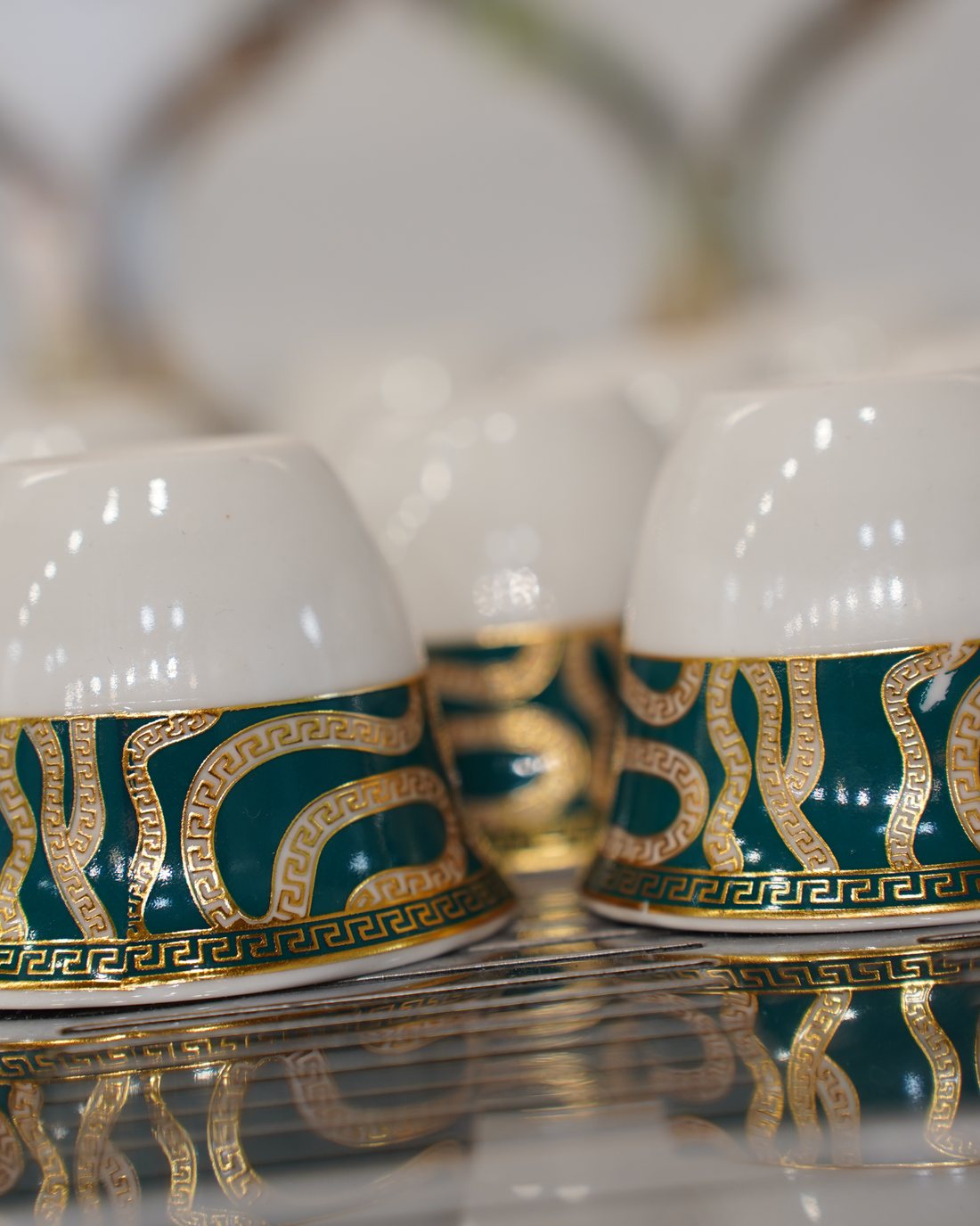 White Yemeni qahwah cups with an emerald-green and gold band, reflected on the glass counter