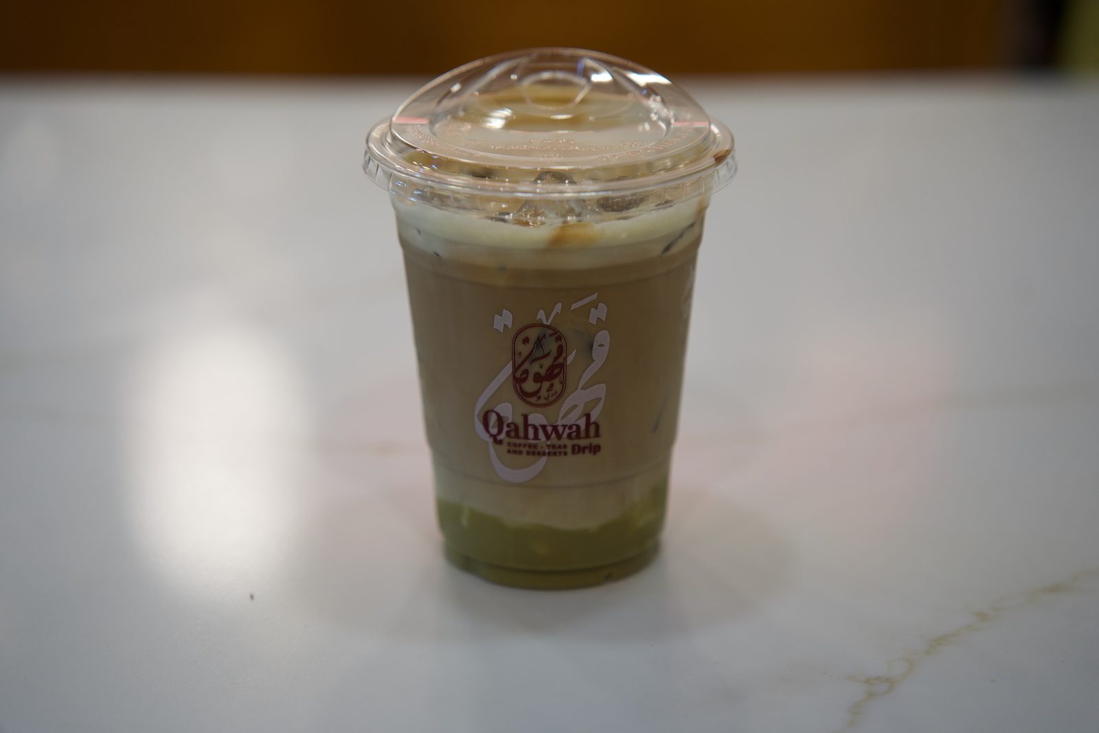 Layered iced matcha latte in a Qahwah Drip cup